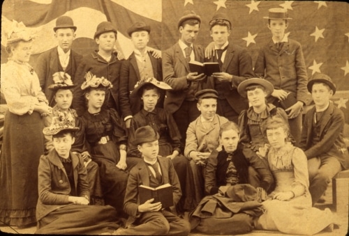 Dressed in their finest wool dresses and serge suits, these 1893 sixth and seventh grade German students gathered in front of an American flag. Many immigrant parents preferred to send their children to church schools where both the old and the new ways were taught in the language of the home.