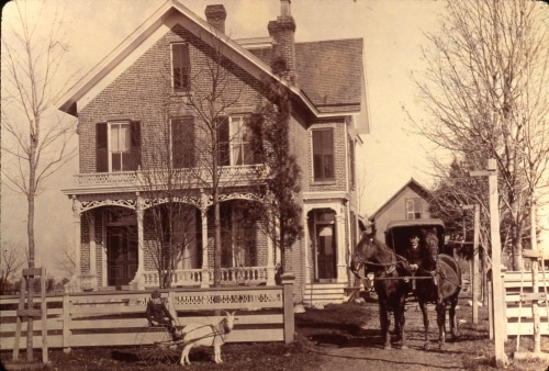 horse-drawn carriage and goat pulling a cart with a boy, in front of brick house