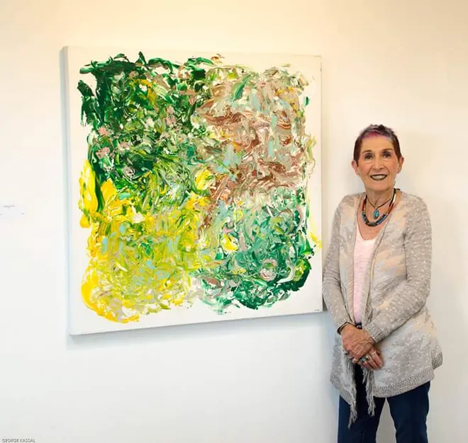 a photo showing the artist next to her work, an abstract canvas showing brilliant greens