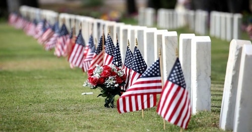 headstones and american flags line the edge of the grass