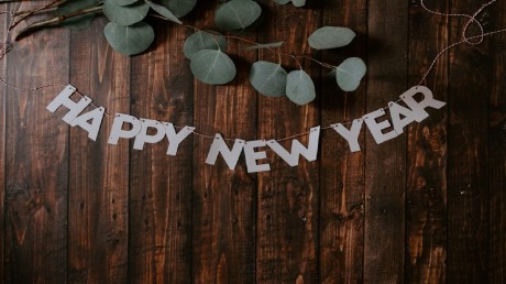 the text happy new year is written with paper letters on top of wooden boards with eucalyptus branches above it